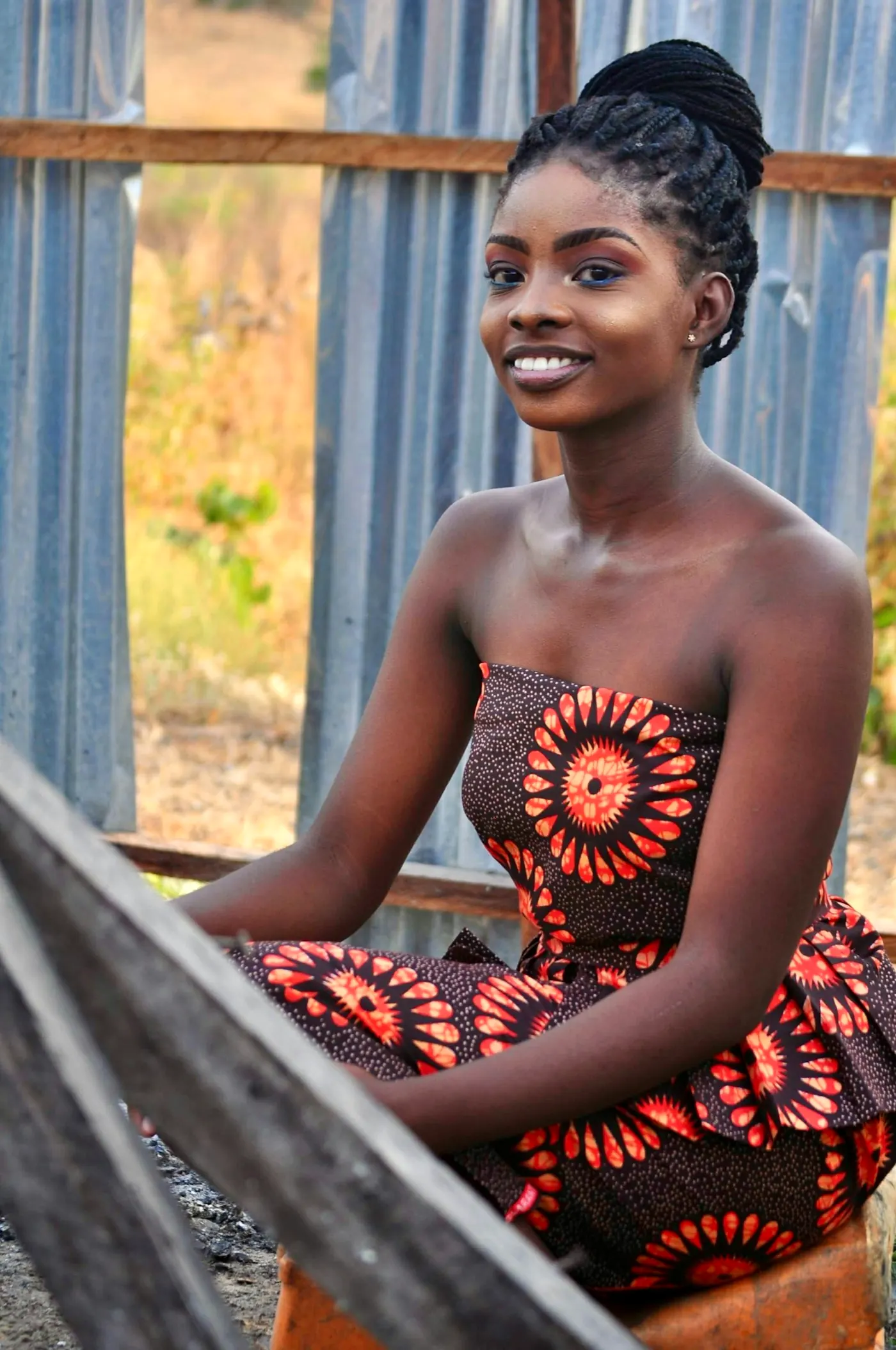 A young woman in a red patterned dress, seated, smiling toward the camera.