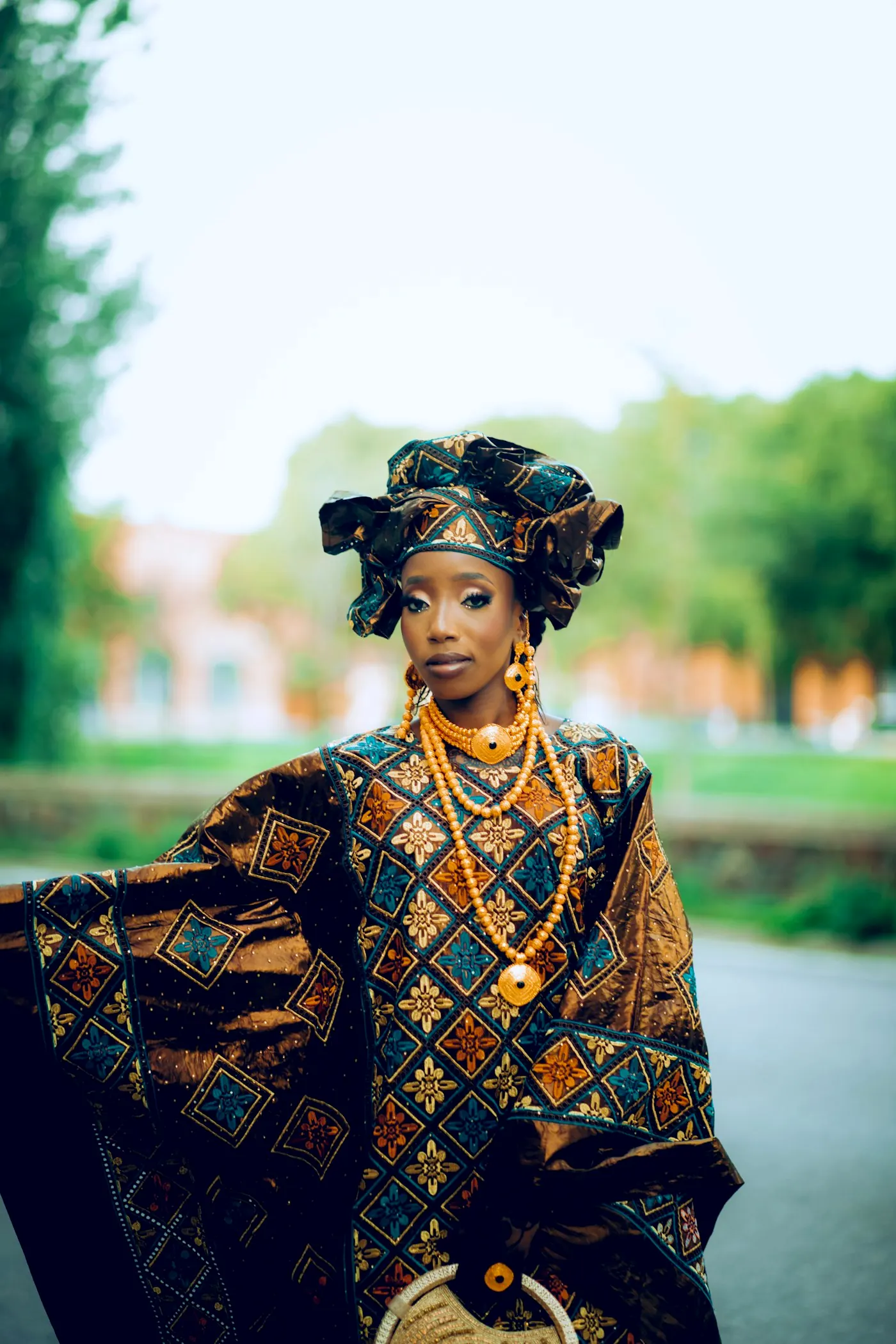 Woman outdoors in an elaborate patterned gown and sculptural headwrap.
