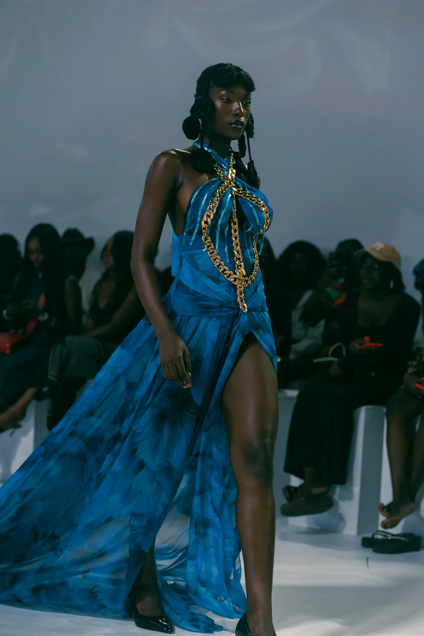 Model in a blue gown with a high slit, walking past a seated audience.