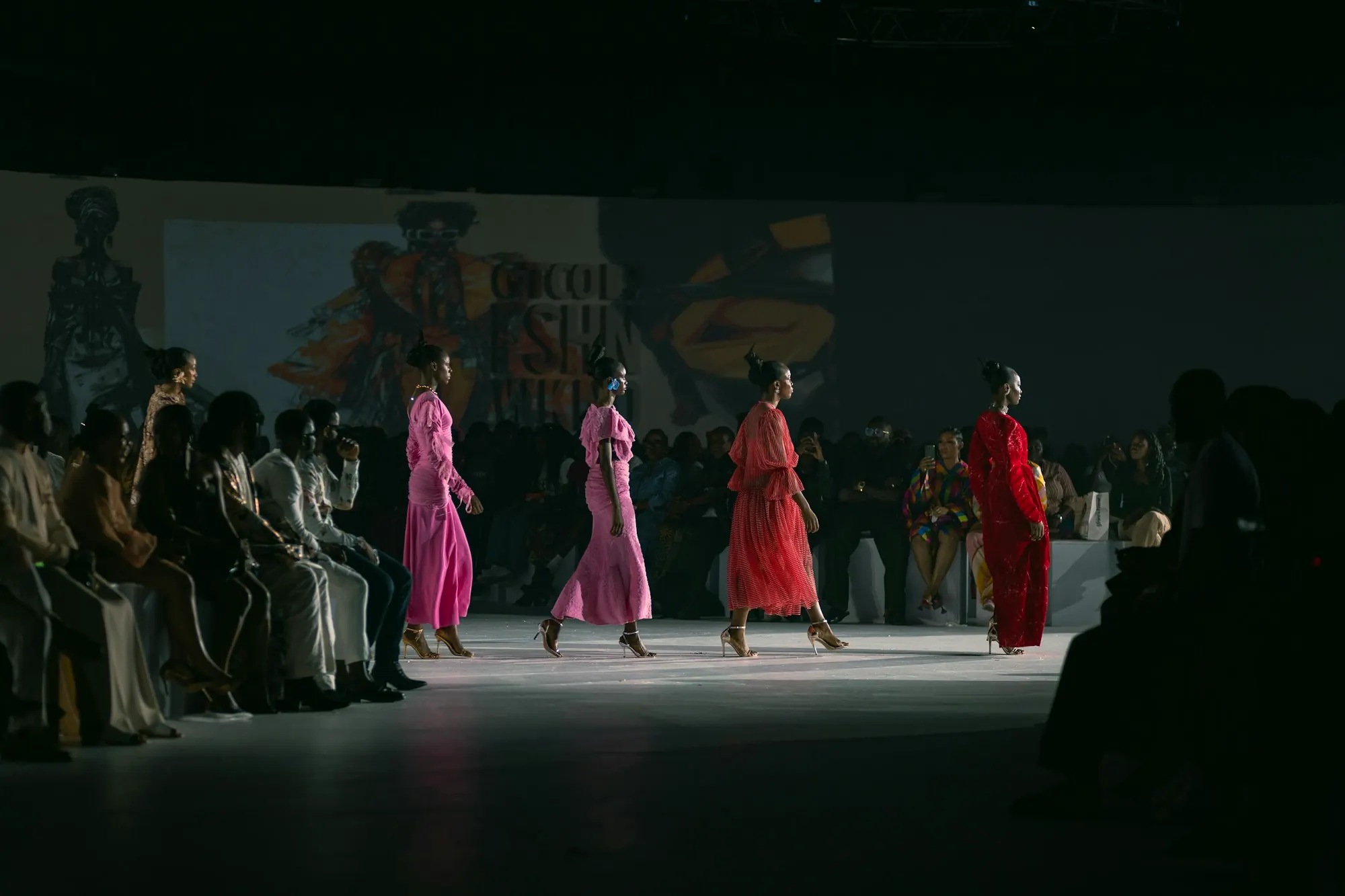 Several models in pink and red gowns walking in a line.