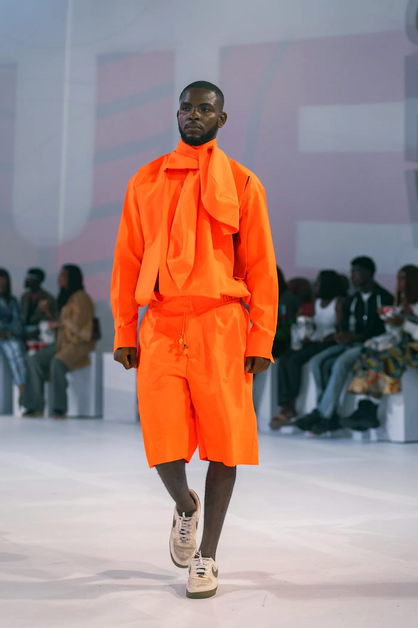 A man in a bright orange ensemble walking a runway.