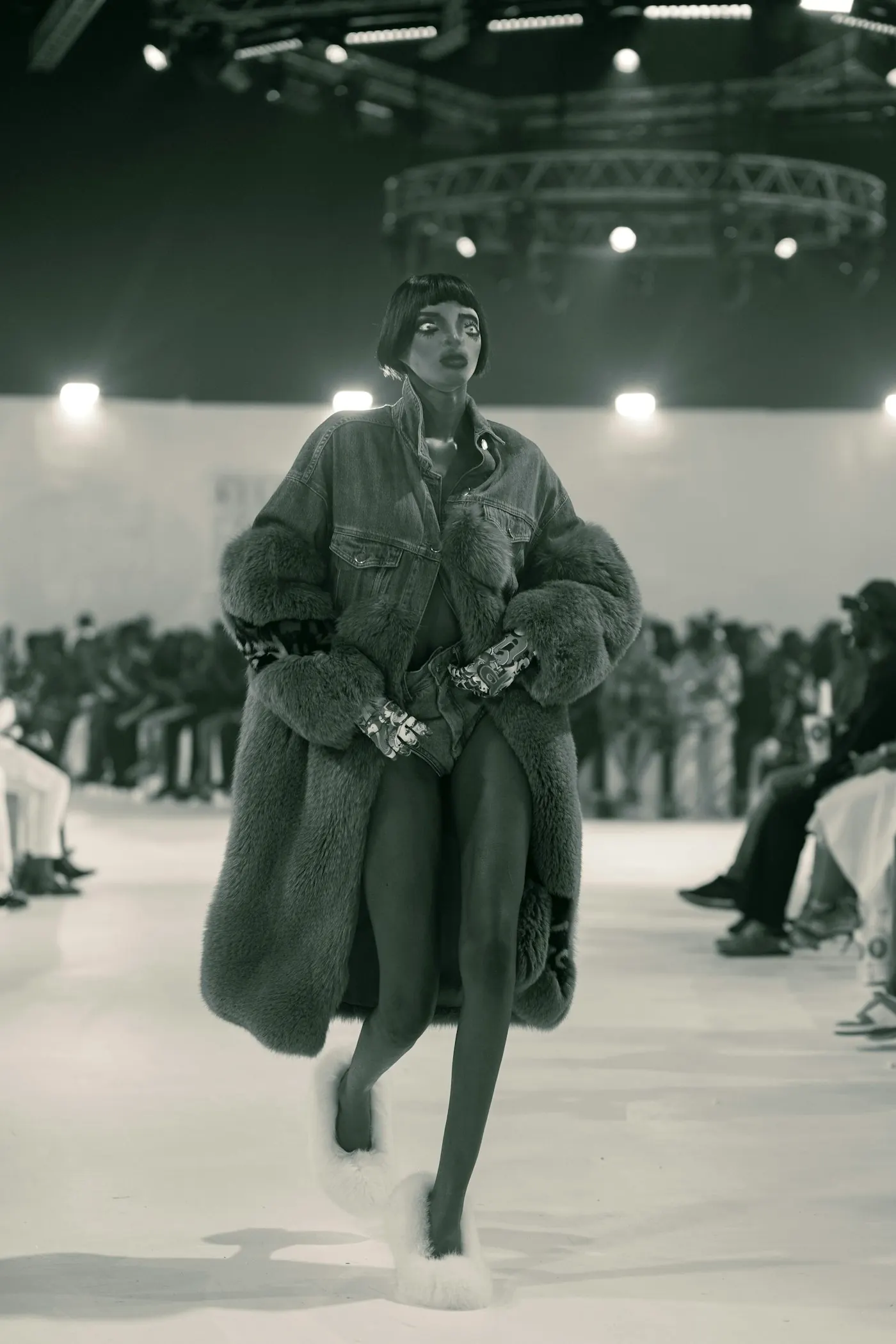 Black and white photograph of a model striding down a runway.