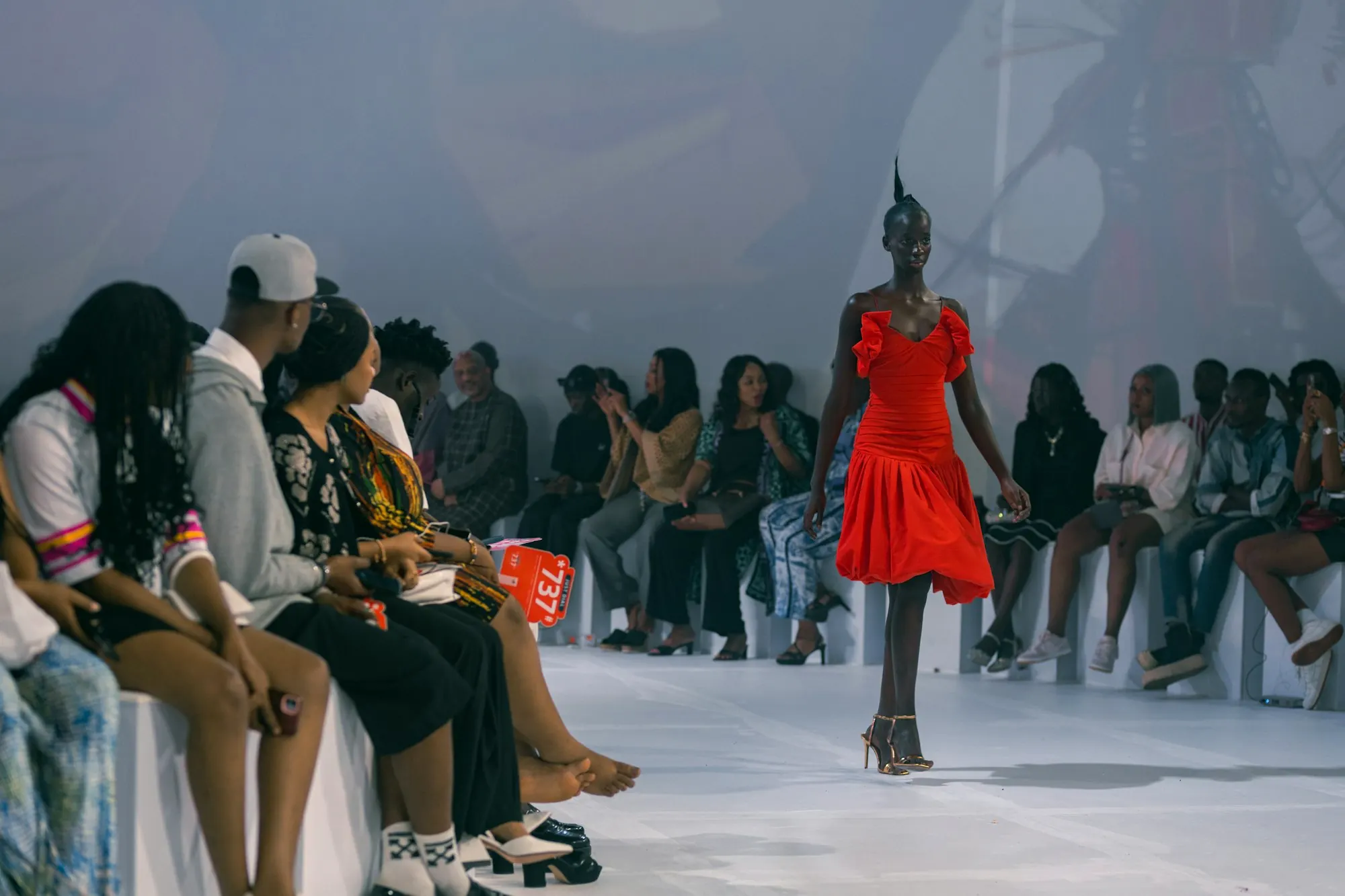 A model in red crossing in front of a seated audience.